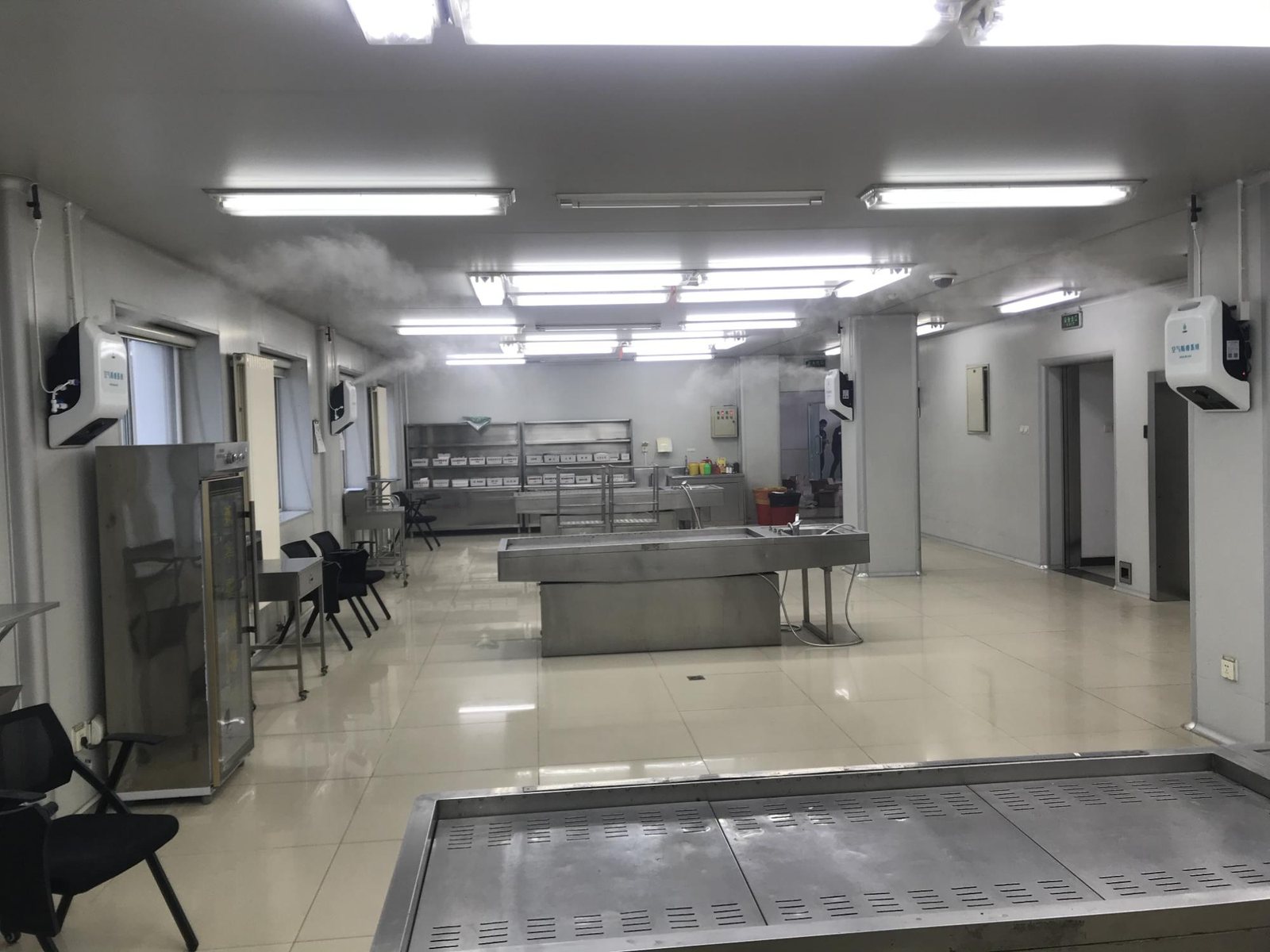 北京市公安局法医中心解剖室内部，可见不锈钢解剖操作台与正在工作的空气消毒喷雾